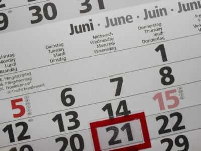 Close-up of a multilingual wall calendar page for June, with weekday headers in German, English, French and Dutch. The dates 12 through 22 are visible across two rows, with the number 21 highlighted by a red rectangular marker overlay. The numbers 5 and 15 appear in red text with country code annotations in small circles next to them.