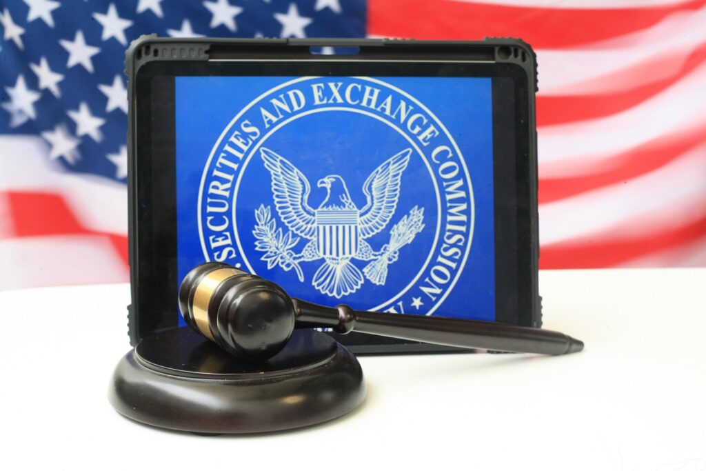 Black gavel resting on a sound block in front of a tablet displaying the Securities and Exchange Commission seal, with an American flag in the background.