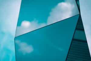 Angular teal-tinted glass panels on a building exterior reflecting blue sky and white clouds, representing the Microsoft Azure cloud platform.