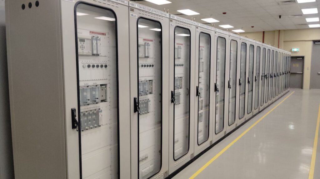 Row of tall server cabinets with glass doors and labeled electrical panels lining a hallway with yellow floor markings.