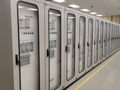 Row of tall server cabinets with glass doors and labeled electrical panels lining a hallway with yellow floor markings.