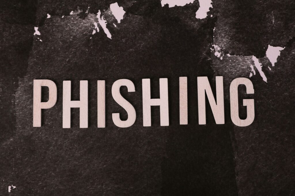 Wooden block letters spelling PHISHING on a dark, mottled black and white textured surface.