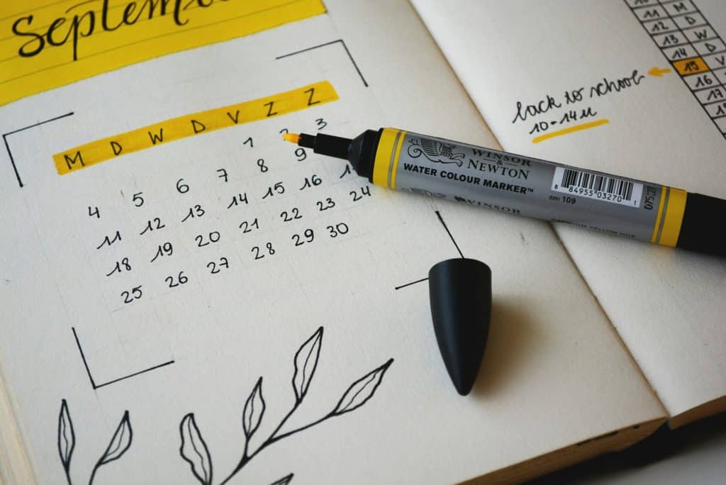 Open notebook with a hand-drawn September calendar under a yellow highlighted heading, with an uncapped yellow Winsor & Newton watercolor marker and its black cap resting on the page.