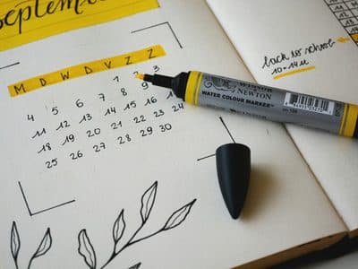 Open notebook with a hand-drawn September calendar under a yellow highlighted heading, with an uncapped yellow Winsor & Newton watercolor marker and its black cap resting on the page.
