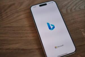 Smartphone lying on a wooden table, its white screen showing the blue Bing logo with the Microsoft logo and wordmark below.